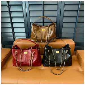 Three quilted chain tote bags in burgundy, brown and black shown on a leather sofa