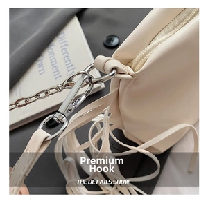 Detailopname van de crèmekleurige plooitas met zilveren metalen haken en kwastjes