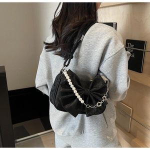Detail view of black bow shoulder bag with pearl accents and flower chain on a model