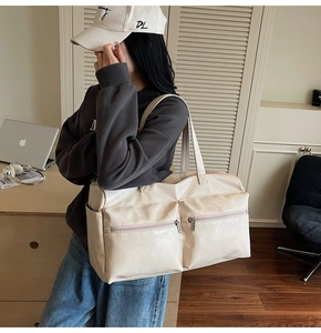 Detail view of a large cream tote bag with dual zipper front pockets and leather texture