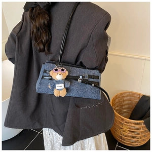 Detail of denim patchwork handbag with black leather straps and cute bear charm accessory