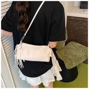 Side view of beige ruched baguette bag with long tassels on a model with white skirt