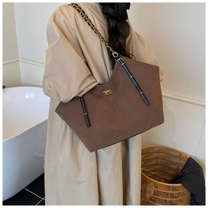 Detail of a large brown quilted suede tote bag featuring a gold twist-lock on a model