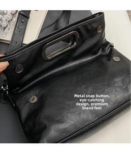 Detail der Magnetschnalle und des polierten Metallgriffs an einer schwarzen Ledertasche