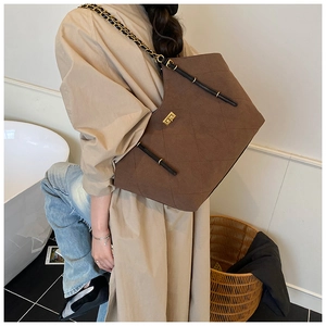 Brown quilted chain tote bag with suede texture shown on shoulder in a lifestyle setting