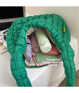 Macro shot of large capacity green quilted cloud bag with umbrella and cosmetics inside
