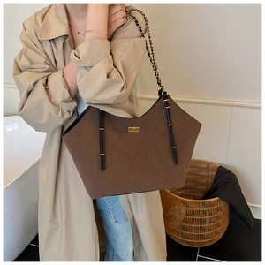 Detail of dark brown suede tote bag with chain strap and quilted stitching on a model