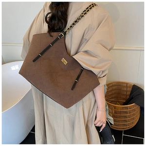 Close-up of brown quilted suede tote bag featuring a golden turn-lock and chain strap