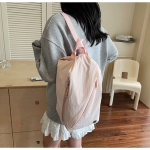 Side view of a light pink nylon backpack with drawstring closure shown on a female model
