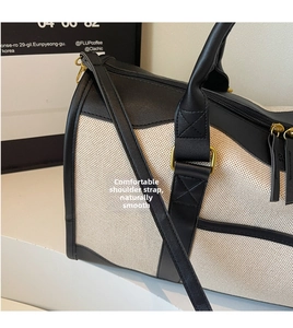 Detail of canvas travel bag featuring reinforced black leather handles and golden metal buckles