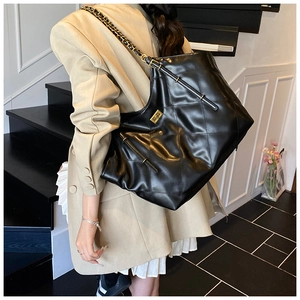 Detail of black quilted leather tote bag with gold chain strap on a fashion model