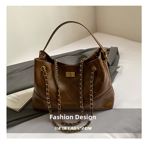 Detail of brown quilted tote bag with gold chain strap and metal lock on a white surface