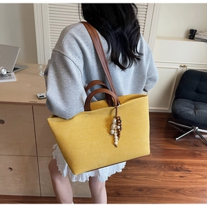 Detail of yellow canvas tote bag featuring brown leather handles and vintage beaded charm