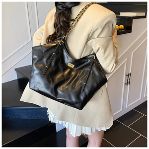 Close-up of black quilted tote bag with gold chain strap and metal turn-lock detail