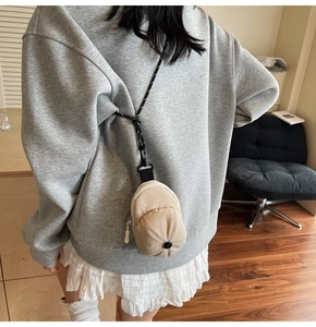 Detailed view of mini hat-shaped beige plaid pouch with zipper and black neck strap