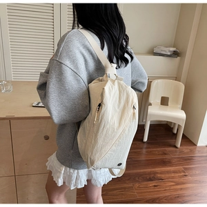 Detail of a beige pleated nylon backpack shown on model in a natural indoor setting