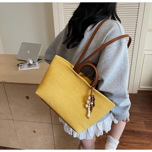 Detail of yellow canvas tote bag with brown leather handles and wooden bead charm accessory