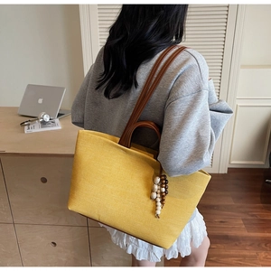 Detail of yellow canvas tote bag with brown leather handles and wood bead charm