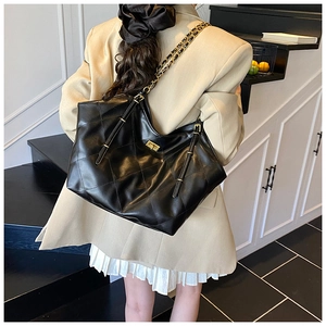 Detail view of black quilted tote bag with gold chain strap and metallic twist lock