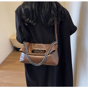 Detail of caramel brown crossbody bag with silver chain and cutout handle worn by a model