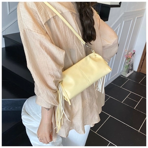 Detail showing the light yellow cylindrical tassel bag with soft leather texture on person