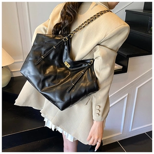 Detail of black quilted chain bag featuring glossy leather texture and gold metal lock