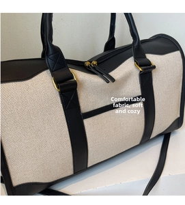 Detail of off-white canvas travel bag with black leather reinforcement and bronze hardware