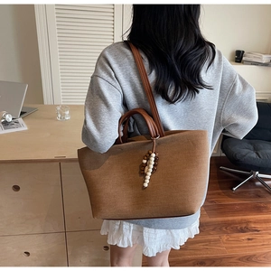 Brown canvas tote bag detail showing leather handles and decorative wooden bead charm