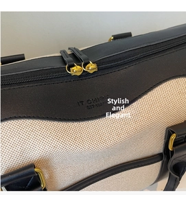 Close-up of cream canvas travel bag with black leather trim and gold metal zippers