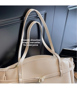Detail of beige lychee textured leather tote bag with long straps and metal buckle accents