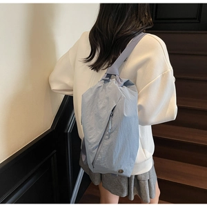 Close-up of light blue nylon crossbody bag on a model showing smooth zipper and logo