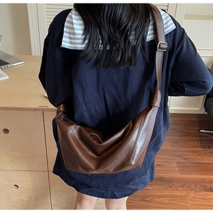 Rear view of a dark brown crescent bag with adjustable wide shoulder strap on model