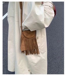 Détail du sac à bandoulière en daim marron à franges porté avec un trench beige