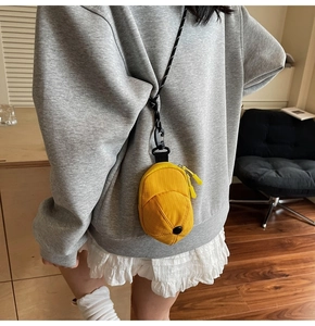 Detailed view of mini yellow hat-shaped nylon crossbody bag with black cord and zippers