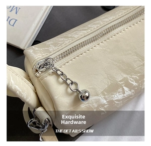 Detailed shot of glossy cream cylinder bag with silver zipper and ball chain charm