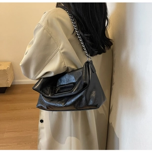 Close-up of black leather pleated chain bag with silver handle worn with a beige trench coat