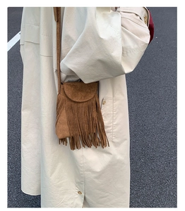 Sac bandoulière bohème en daim marron avec franges porté par un mannequin en trench