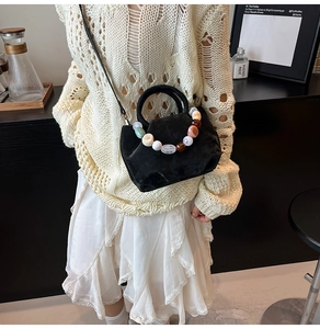Détail d'un sac seau en daim noir avec poignée en perles colorées porté par un mannequin
