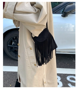 Détail du sac bandoulière noir à longues franges porté avec un trench-coat beige