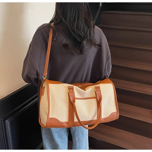 Detail of canvas travel bag with brown leather trim carried on shoulder in indoor setting