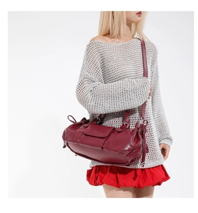 Detail of dark red pleated leather baguette bag with metal buckle and side drawstring