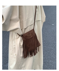 Détail d'un sac bandoulière en daim marron foncé à franges sur un trench-coat beige