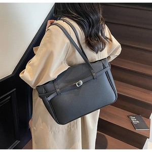 Detail of black pebbled leather tote bag with gold buckle on a model in a trench coat