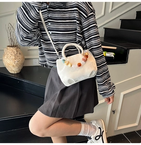 Détail du sac bandoulière crème avec perles décoratives en résine colorée sur la poignée
