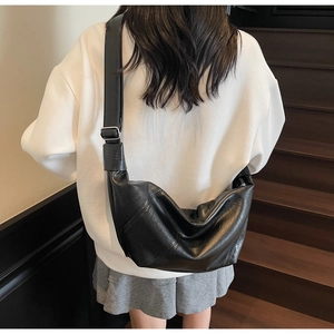 Detail of black synthetic leather dumpling bag with silver buckle and adjustable strap