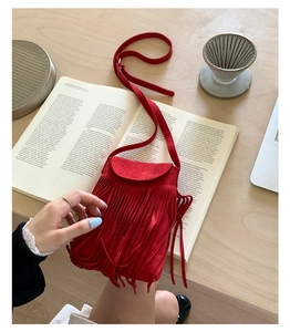 Détail du sac à bandoulière en daim rouge avec franges sur un livre ouvert