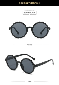 Detail view of round scalloped petal sunglasses with black frames and metal rivets