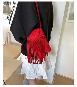 Gros plan sur un sac bandoulière en daim rouge mat avec détails de franges et rabat