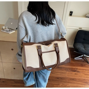 Detail of canvas travel tote with brown leather straps shown on person's shoulder