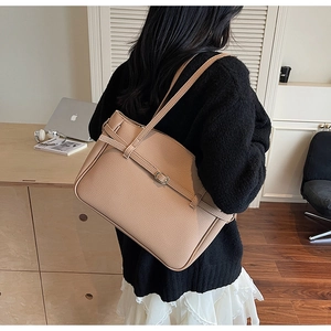 Detailed shot of camel leather tote bag showing grainy texture and decorative buckle straps